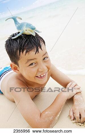 A Boy Laying On The Sand At The Water's Edge With A Toy Whale On His Head; Kailua, Oahu, Hawaii, United States Of America View Large Photo Image Stock Photograph - A Boy Laying On The Sand At The Water's Edge With A Toy Whale On His Head; Kailua, Oahu, Hawaii, United States Of America. Fotosearch