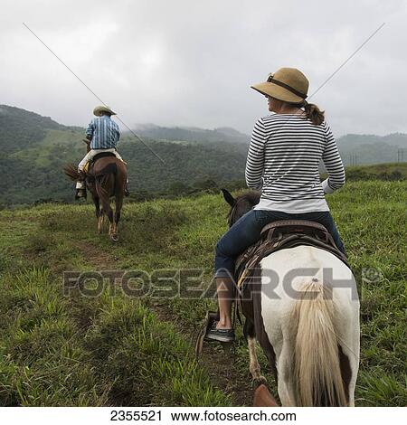 Stock Image - A Man And Woman Riding Horseback Through The Hills; Zacapa, Guatemala. Fotosearch