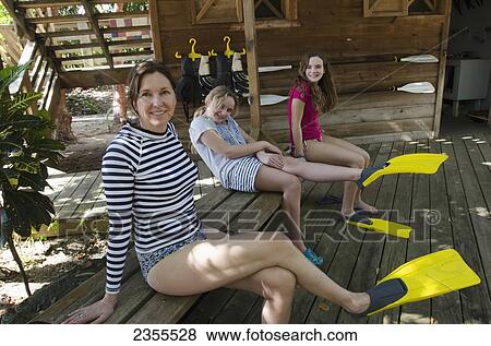 Stock Photo - A Mother And Two Daughters Sit On A Wooden Bench With Flippers On Their Feet; Utila Island, Honduras. Fotosearch