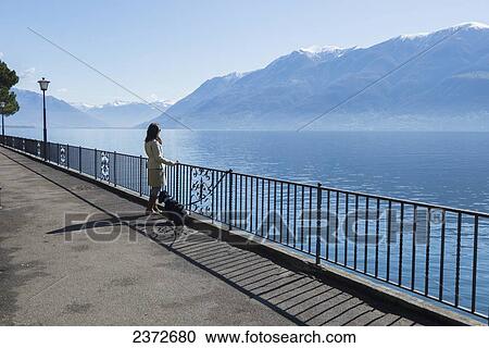 A Woman And Her Dog Stand Against A Railing At The Edge Of Lake Maggiore; Brissago, Ticino, Switzerland View Large Photo Image Stock Image - A Woman And Her Dog Stand Against A Railing At The Edge Of Lake Maggiore; Brissago, Ticino, Switzerland. Fotosearch