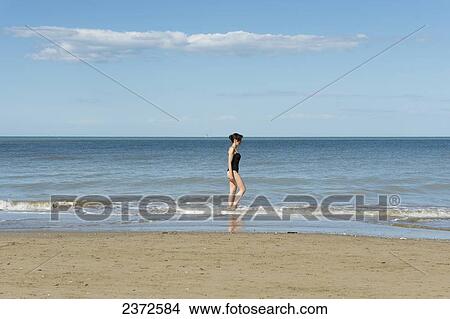 Picture - A Woman In A Bathing Suit Walks In The Shallow Water On The Beach; Rimini, Emilia-Romagna, Italy. Fotosearch