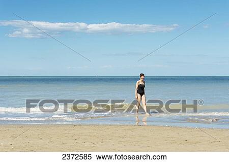 Stock Photography - A Woman In A Bathing Suit Walks In The Shallow Water On The Beach; Rimini, Emilia-Romagna, Italy. Fotosearch