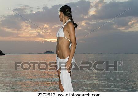 A woman in a white bikini and a tropical flower in her hair poses in the water at sunset; Honolulu, Hawaii, United States of America View Large Photo Image Stock Image - A woman in a white bikini and a tropical flower in her hair poses in the water at sunset; Honolulu, Hawaii, United States of America. Fotosearch