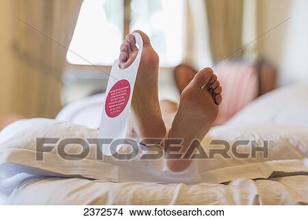 A Woman's Feet At The End Of A Bed With The Door Hanger Hanging From Her Toes; Sestri Levante, Liguria, Italy View Large Photo Image Picture - A Woman's Feet At The End Of A Bed With The Door Hanger Hanging From Her Toes; Sestri Levante, Liguria, Italy. Fotosearch