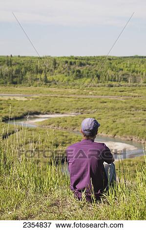 Man Sitting On A Cliff Overlooking A Lush River Valley With Blue Sky; Calgary, Alberta, Canada View Large Photo Image Stock Photo - Man Sitting On A Cliff Overlooking A Lush River Valley With Blue Sky; Calgary, Alberta, Canada. Fotosearch