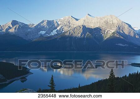 Mountain Range Reflecting In A Lake At Sunrise With Blue Sky; Kananaskis Country, Alberta, Canada View Large Photo Image Stock Photo - Mountain Range Reflecting In A Lake At Sunrise With Blue Sky; Kananaskis Country, Alberta, Canada. Fotosearch