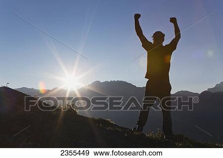 Silhouette Of Male Hiker Standing On Top Of Mountain Ridge With Arms Up In The Air, With Sun Burst Breaking Over Mountain Range At Sunrise With Blue Sky; Kananaskis Country, Alberta, Canada View Large Photo Image Stock Photo - Silhouette Of Male Hiker Standing On Top Of Mountain Ridge With Arms Up In The Air, With Sun Burst Breaking Over Mountain Range At Sunrise With Blue Sky; Kananaskis Country, Alberta, Canada. Fotosearch