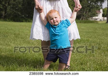 Stock Photo - A baby with red hair learning to walk and holding onto his mother's hands; Stony Plain, Alberta, Canada. Fotosearch