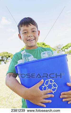 Stock Photo - A boy holding a recyclable trash bin with empty plastic bottles at a park; Honolulu, Oahu, Hawaii, United States of America. Fotosearch