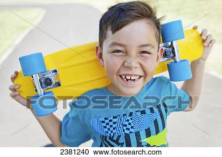 Stock Image - A boy holding his skateboard on a bike and skate path; Honolulu, Oahu, Hawaii, United States of America. Fotosearch