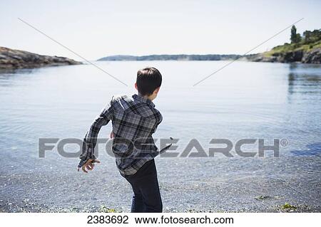 Stock Image - A boy throws rocks into the water; Victoria, British Columbia, Canada. Fotosearch