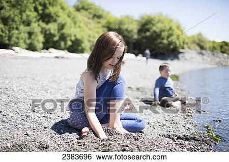 Stock Photograph - A brother and sister sit in the sand at the water's edge; Victoria, British Columbia, Canada. Fotosearch