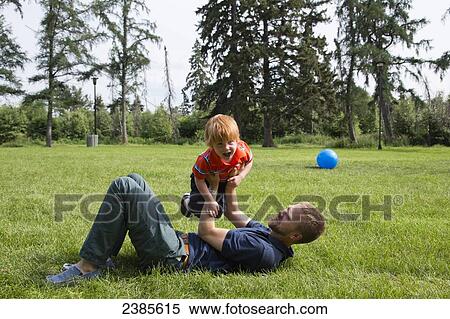 Stock Photography - A father plays with his young son on a grass field; Stony Plain, Alberta, Canada. Fotosearch