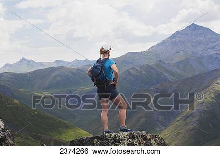 Stock Photograph - A female hiker stands looking over the landscape of mountains and valleys; Yukon, Canada. Fotosearch