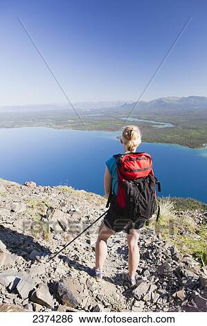 Stock Photograph - A female hiker stands looking over the landscape of mountains and lakes in the valley; Yukon, Canada. Fotosearch