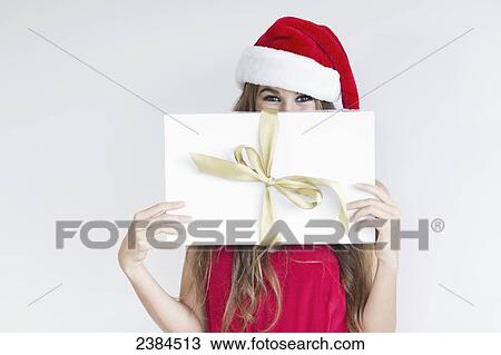 Stock Image - A girl dressed in a red shirt and santa hat holds a wrapped gift; Hawaii, United States of America. Fotosearch