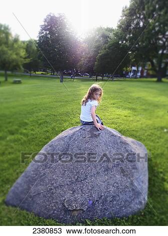 Stock Image - A girl sitting on a rock in the Plains of Abraham city park on a summer day; Quebec City, Quebec, Canada. Fotosearch