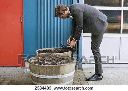 Stock Image - A man dressed in a suit tying his shoelace; British Columbia, Canada. Fotosearch