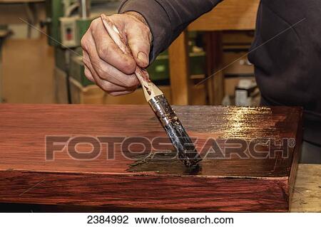 Stock Image - A man paints stain onto wood; Nanaimo, British Columbia, Canada. Fotosearch