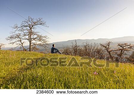 Stock Image - A man sitting in contemplation during a hike at sunset on Mount Tzouhalem on Vancouver Island; British Columbia, Canada. Fotosearch