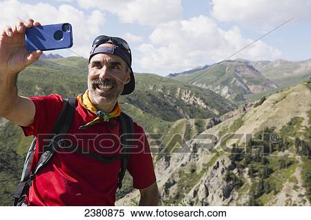 Stock Photography - A man takes a self portrait with his cell phone camera in the mountains; Haines Junction, Yukon, Canada. Fotosearch