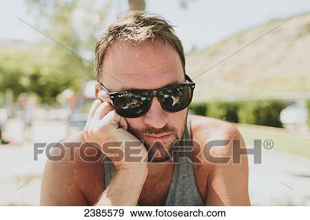 A man wearing sunglasses sits with his head leaning on his hand; Peachland, British Columbia, Canada View Large Photo Image Stock Photo - A man wearing sunglasses sits with his head leaning on his hand; Peachland, British Columbia, Canada . Fotosearch