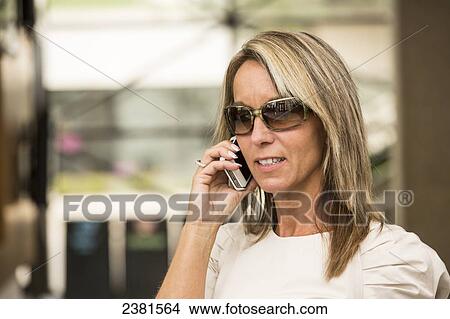 Picture - A mature professional businesswoman in a downtown office environment using cell phone; Edmonton, Alberta, Canada. Fotosearch