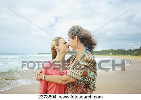 Picture - A mother and daughter together on the beach at the water's edge; Kauai, Hawaii, United States of America. Fotosearch