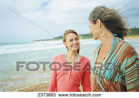 Stock Image - A mother and daughter walking together on the beach at the water's edge; Kauai, Hawaii, United States of America. Fotosearch
