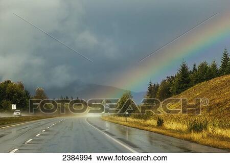 Picture - A rainbow comes from the storm clouds right onto the highway ahead; Parksville, British Columbia, Canada. Fotosearch