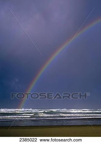 Stock Image - A rainbows arcs over the surf; Winchester Bay, Oregon, United States of America. Fotosearch