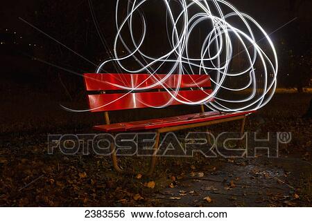 Stock Photograph - A red park bench in autumn with swirls of white light in the sky around it; Locarno, Ticino, Switzerland. Fotosearch