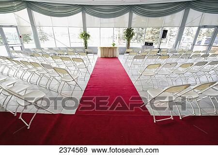 Stock Photo - A room set up for a wedding ceremony with red carpet and white chairs; Edmonton, Alberta, Canada. Fotosearch