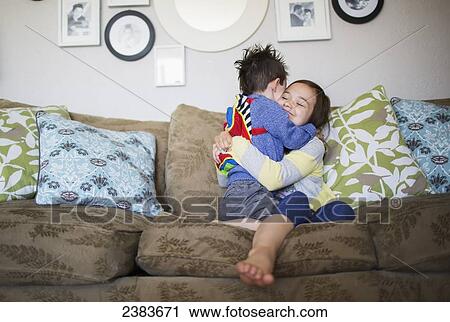 Stock Image - A sister and brother in an embrace on the couch at home; Victoria, British Columbia, Canada. Fotosearch