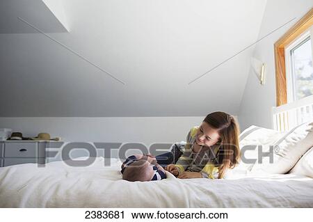 Stock Image - A sister playing with her baby brother on a bed at home; Victoria, British Columbia, Canada. Fotosearch