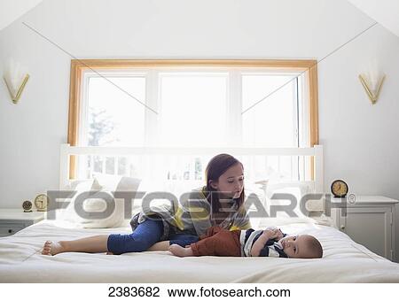 Stock Image - A sister playing with her baby brother on a bed at home; Victoria, British Columbia, Canada. Fotosearch
