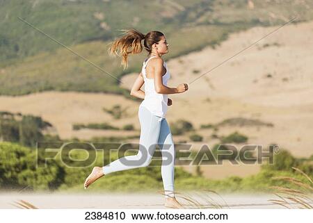 Stock Image - A woman jogging barefoot on the beach; Tarifa, Cadiz, Andalusia, Spain. Fotosearch