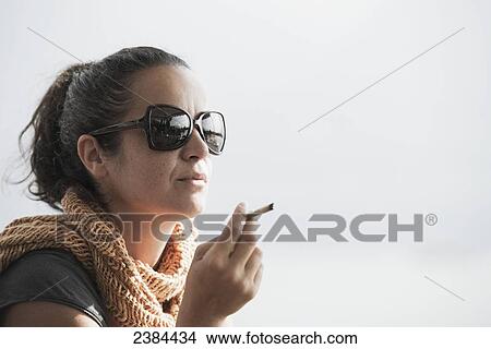 Picture - A woman wearing sunglasses and smoking a cigarette; Locarno, Ticino, Switzerland. Fotosearch