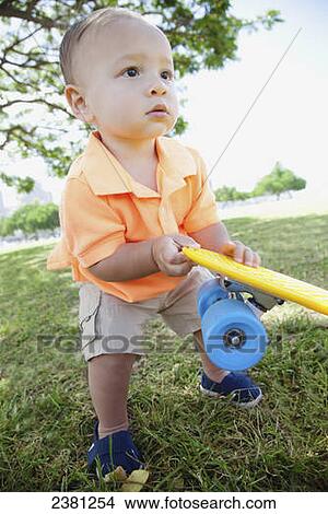 A young boy holding a skateboard at a park; Honolulu, Oahu, Hawaii, United States of America View Large Photo Image Picture - A young boy holding a skateboard at a park; Honolulu, Oahu, Hawaii, United States of America. Fotosearch