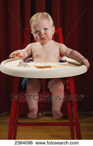 Stock Photo - A young boy sits in his highchair eating a meal; Alberta, Canada. Fotosearch