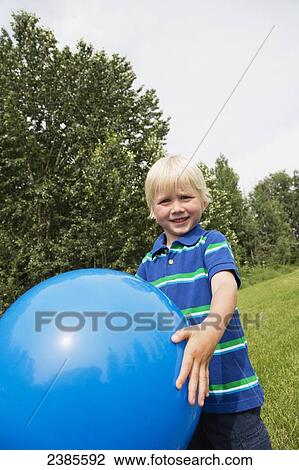 Stock Image - A young boy with blond hair plays with a large blue ball on the grass; Stony Plain, Alberta, Canada. Fotosearch