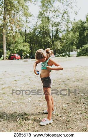 Stock Photo - A young girl applies sunscreen on her skin; Peachland, British Columbia, Canada. Fotosearch