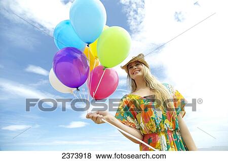 A young woman in a floral dress holding a bundle of colourful balloons; Kauai, Hawaii, United States of America View Large Photo Image Stock Photo - A young woman in a floral dress holding a bundle of colourful balloons; Kauai, Hawaii, United States of America. Fotosearch
