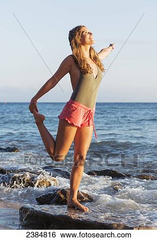 Stock Photograph - A young woman stretching on a wet rock at the water's edge; Tarifa, Cadiz, Andalusia, Spain. Fotosearch
