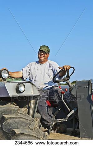 Agriculture - A farmer driving a tractor during potato planting operations at a local family produce farm / Little Compton, Rhode Island, USA. View Large Photo Image Stock Photograph - Agriculture - A farmer driving a tractor during potato planting operations at a local family produce farm / Little Compton, Rhode Island, USA.. Fotosearch