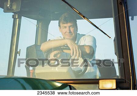 Stock Photo - Agriculture - A farmer sitting in the cab of his John Deere tractor in late afternoon sunlight / near Hoffman, Minnesota, USA.. Fotosearch