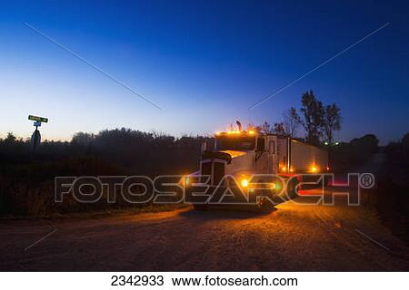 Stock Image - Agriculture - A grain truck at a country road intersection at dusk in route to a grain elevator with a load of freshly harvested corn / near Northland, Minnesota, USA.. Fotosearch