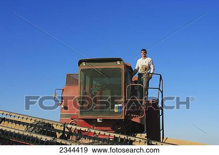 Stock Photo - Agriculture - A young farmer stands on an old sidehill combine during the barley harvest / near Esparto, California, USA.. Fotosearch
