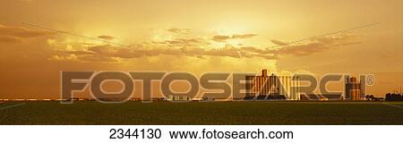 Stock Image - Agriculture - Grain elevators and an early growth corn field in late afternoon light / Johnson City, Kansas, USA.. Fotosearch