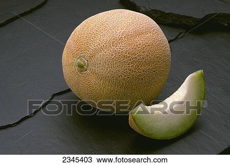 Stock Image - Agriculture - Produce, Galia type green fleshed melon, on black slate.. Fotosearch